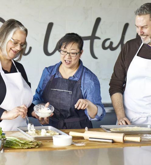 three people wearing aprons discuss cooking items on counter in front of them