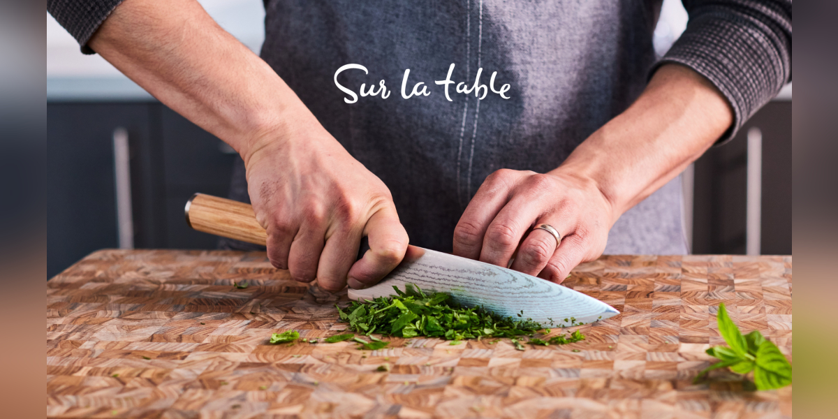 Man cutting green onion with a Sur La Table apron on