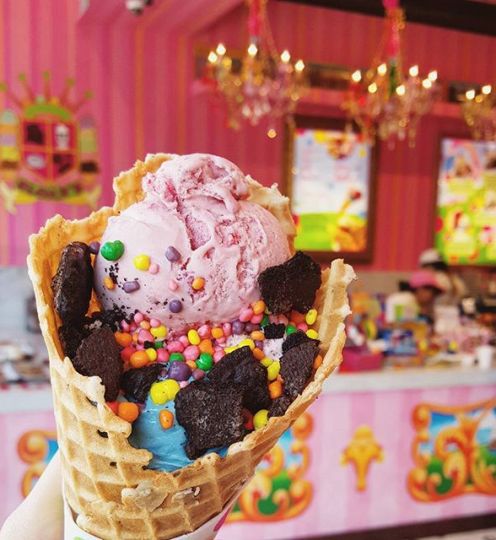 pink ice cream in a waffle cone covered in sprinkles and chocolate crumbs
