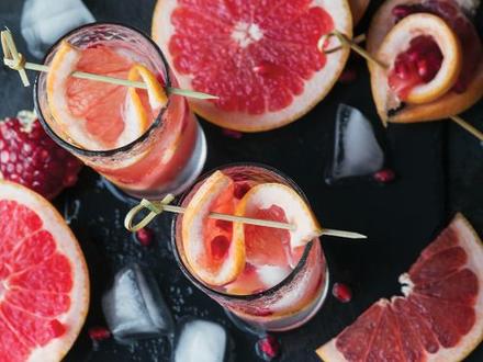 aerial view of two cocktails with citrus wedges on top and surrounded by cut up citrus on dark table