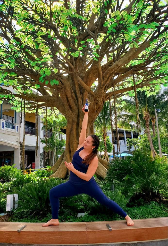Female yoga instructor striking yoga pose with a beer in-hand