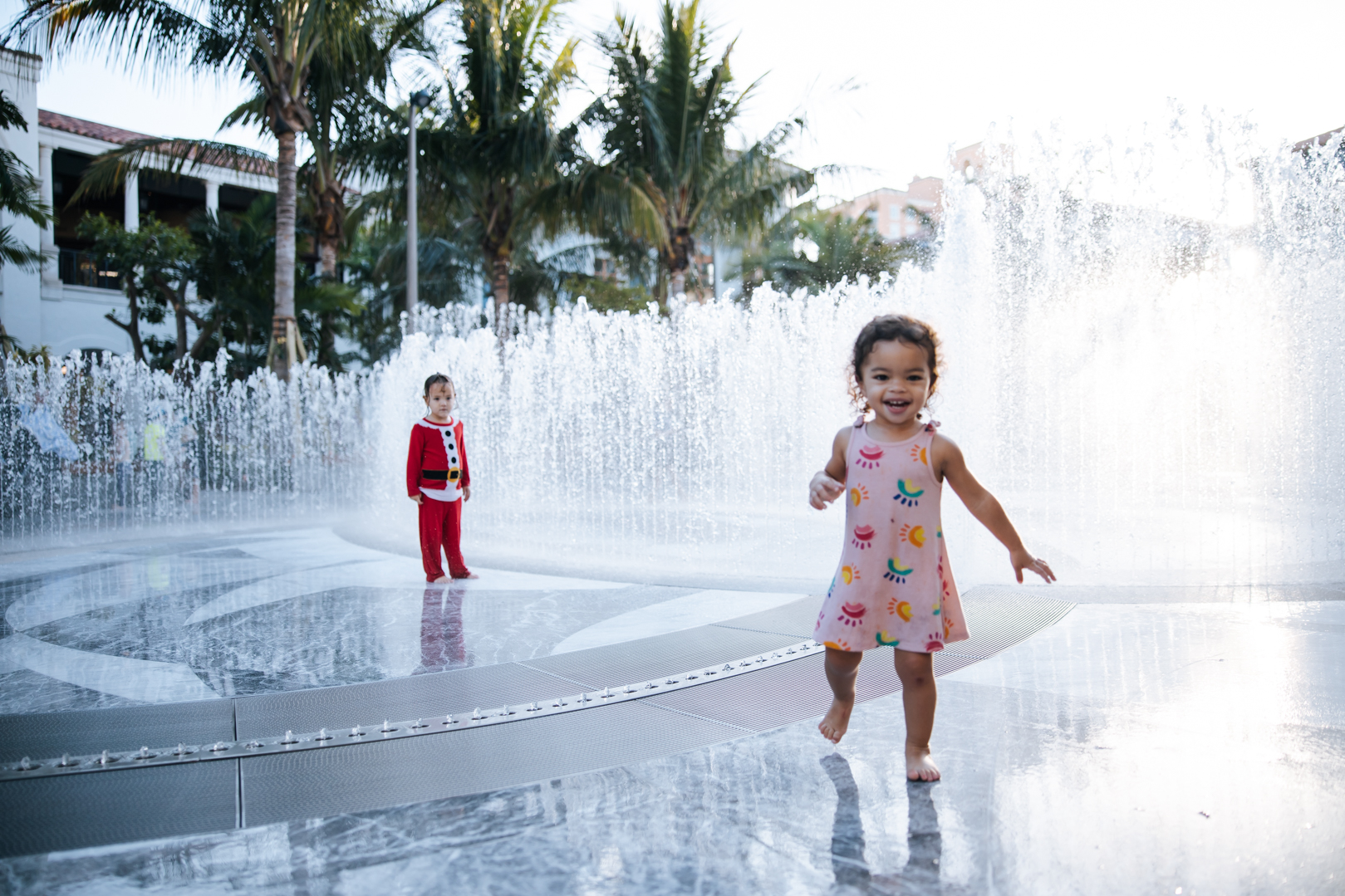 Two toddlers smiling walking through water fountain 