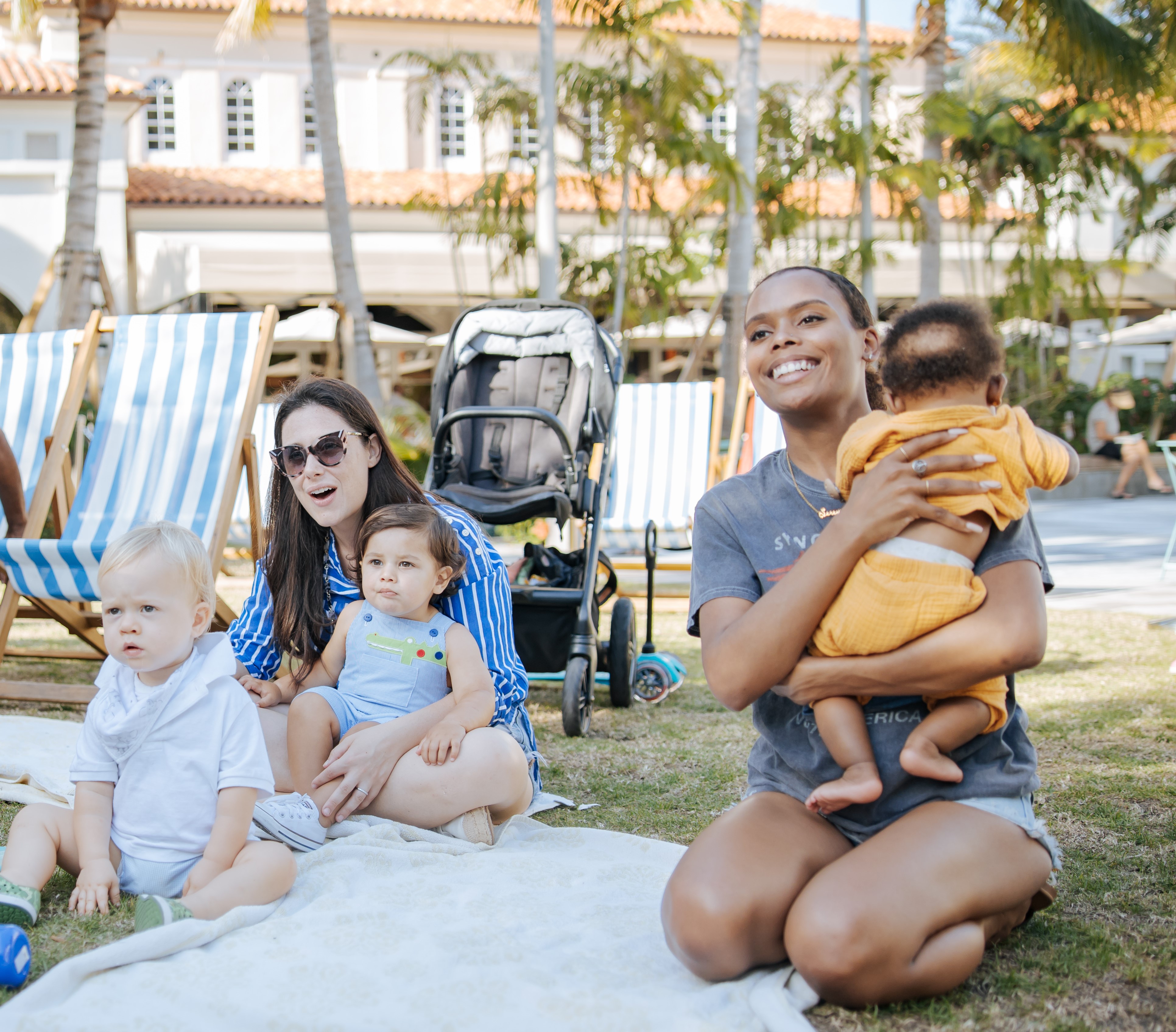 two moms sitting on a blanket in the grass with their babies 