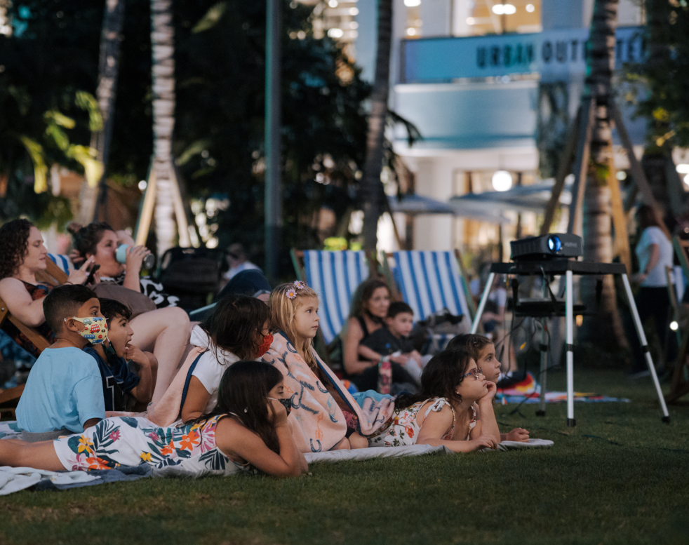 Little kids laying on a lawn watching an outdoor movie 