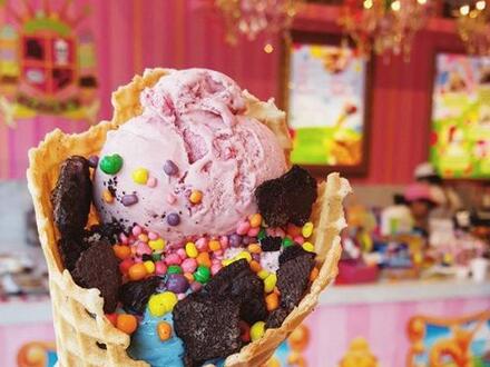 pink ice cream in a waffle cone covered in sprinkles and chocolate crumbs