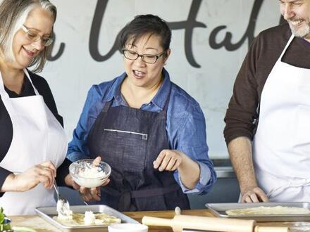 three people wearing aprons discuss cooking items on counter in front of them