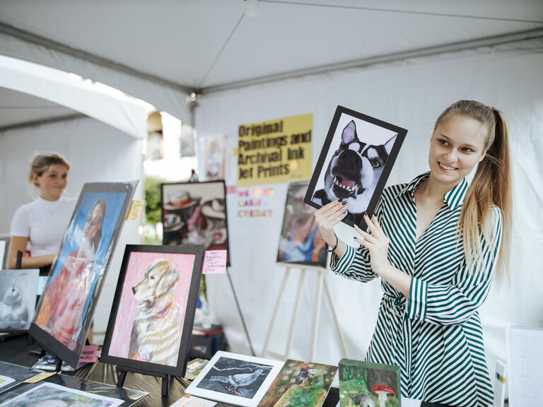 woman holds up framed picture of dog at art show