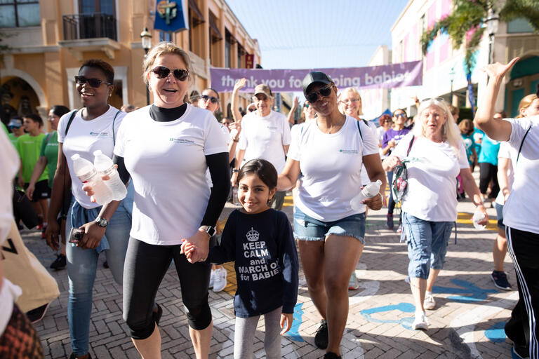 group of people wearing matching white t-shirts walking towards camera with a woman holding child's hand in the foreground