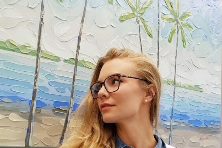 Female artist standing in front of her paintings of palm trees 