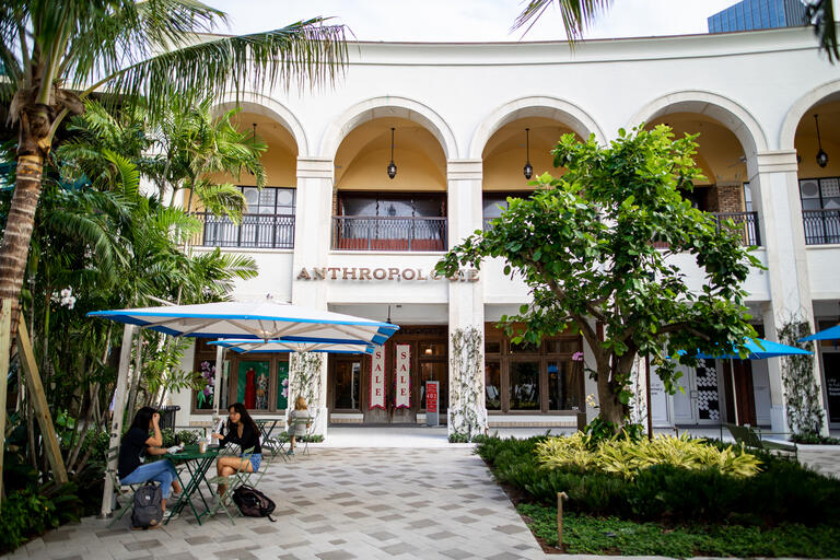 Two girls sitting at outdoor tables under umbrellas in front of Anthropologie 