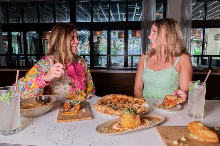 two women at a bar with food and drinks