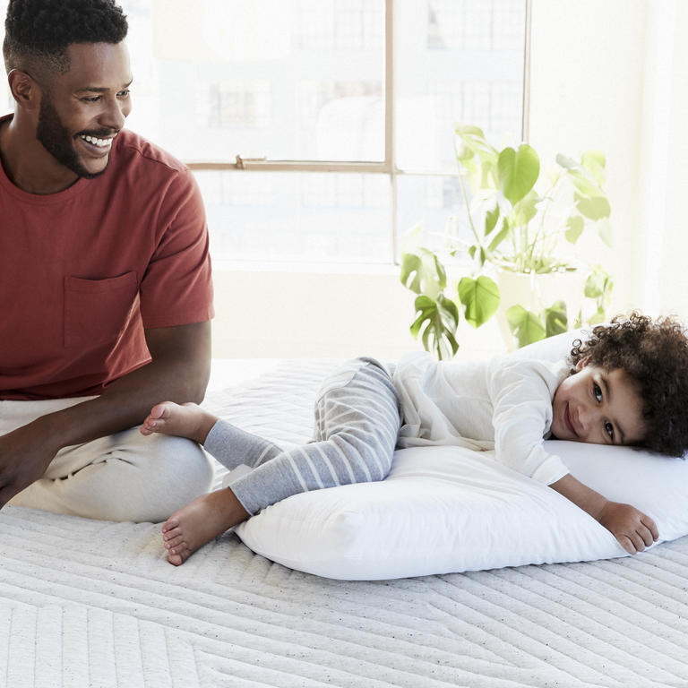 Little boy laying on pillow with father sitting next to him