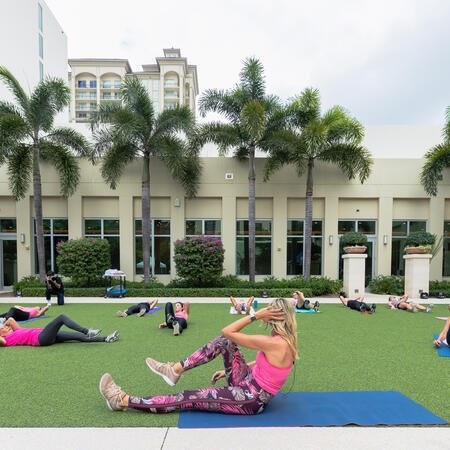 women on yoga mats work out with palm trees in background