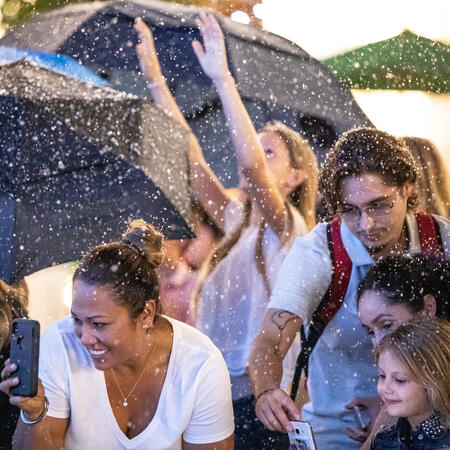 People smile and reach for snow while under umbrellas